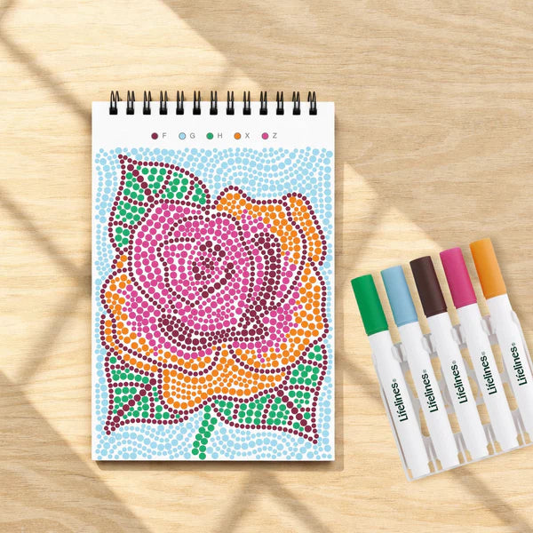 Coloring book with a colorful rose design and markers on a wooden surface