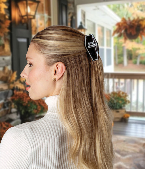Woman with a coffin-shaped hair clip in her hair, standing in a decorated outdoor setting.