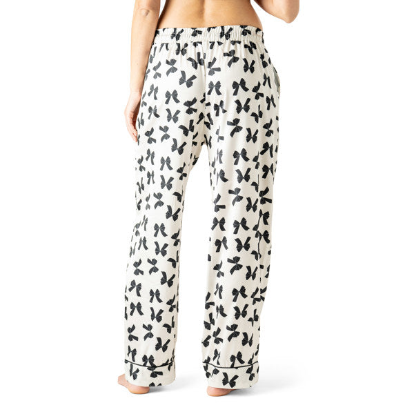 White pajama pants with black bow pattern worn by a person on a white background