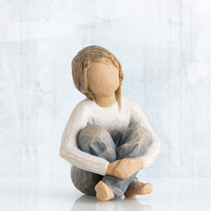 Figure of seated girl in cream shirt and blue jeans, with arms wrapped around knees
