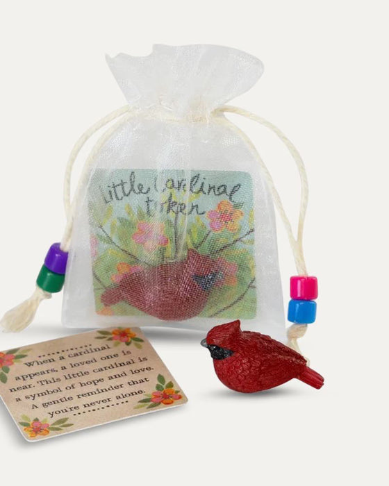 A small red cardinal figurine displayed next to its floral message card and a sheer white drawstring gift bag with colorful beads, on a light cream background.