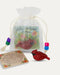A small red cardinal figurine displayed next to its floral message card and a sheer white drawstring gift bag with colorful beads, on a light cream background.