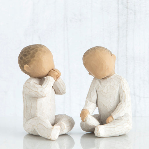 Two ceramic figures of children sitting and facing each other on a white background