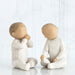 Two ceramic figures of children sitting and facing each other on a white background