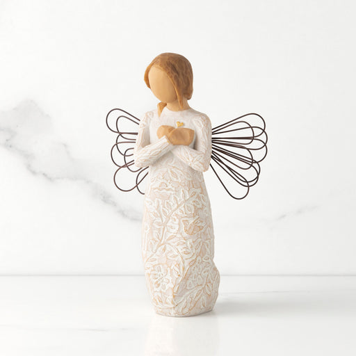 Standing angel in cream dress with wire wings, with crossed hands under small gold-leaf heart. Dress carved with symbols of nature