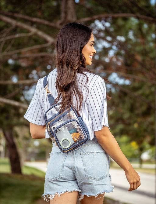 Woman wearing a clear crossbody bag outdoors with trees in the background