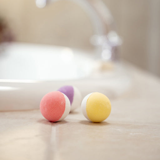 Three colorful bath bombs on a bathroom counter with a blurred background