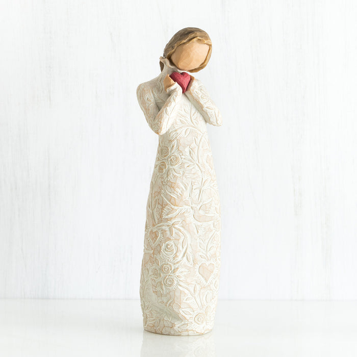 Standing figure in cream dress with ruffled neck, holding red heart in hands; dress extensively carved with hearts, flowers and birds