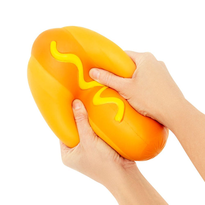Hand holding a squishy toy shaped like a hot dog with mustard on a white background