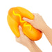 Hand holding a squishy toy shaped like a hot dog with mustard on a white background