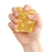 Hand holding a glittery gold square object against a white background