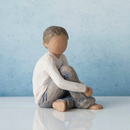 Wooden figurine of a child sitting on a reflective surface with a blue background