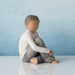 Wooden figurine of a child sitting on a reflective surface with a blue background