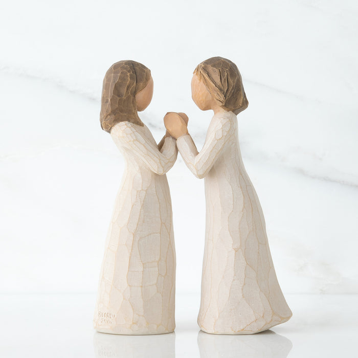 Two standing, separate figures in cream dresses facing each other, with hands that interlock together. Hands of one figure fit into hands of other figure