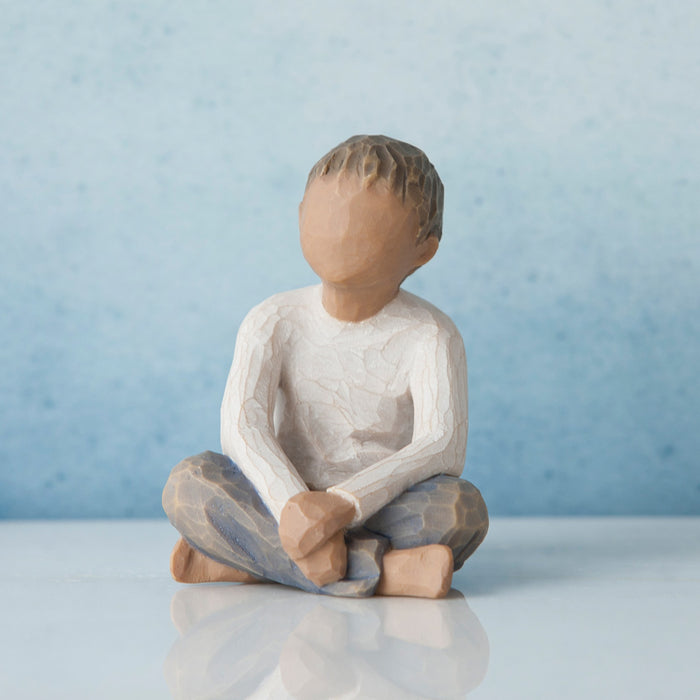 Ceramic figurine of a child sitting cross-legged on a reflective surface with a light blue background