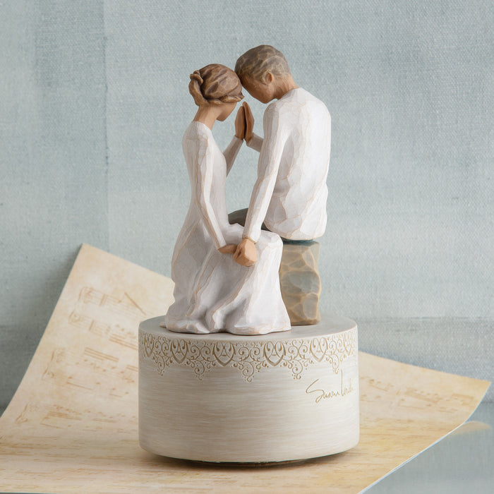 Statue of a couple in a romantic pose on a decorative base with a light gray background