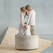 Statue of a couple in a romantic pose on a decorative base with a light gray background