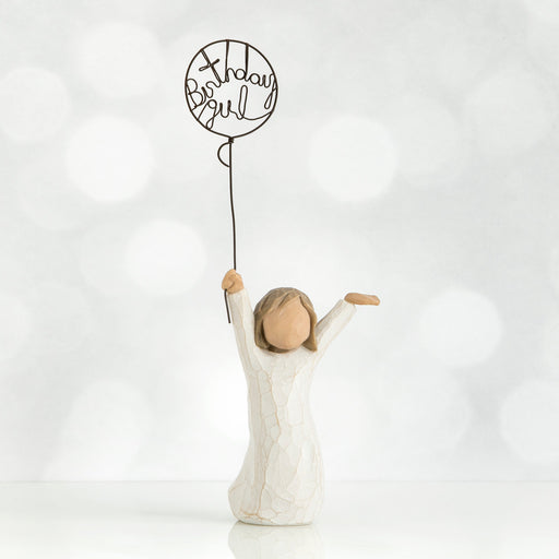 Standing figure in cream dress, holding wire ballon with the words 'birthday girl' written in wire inside it