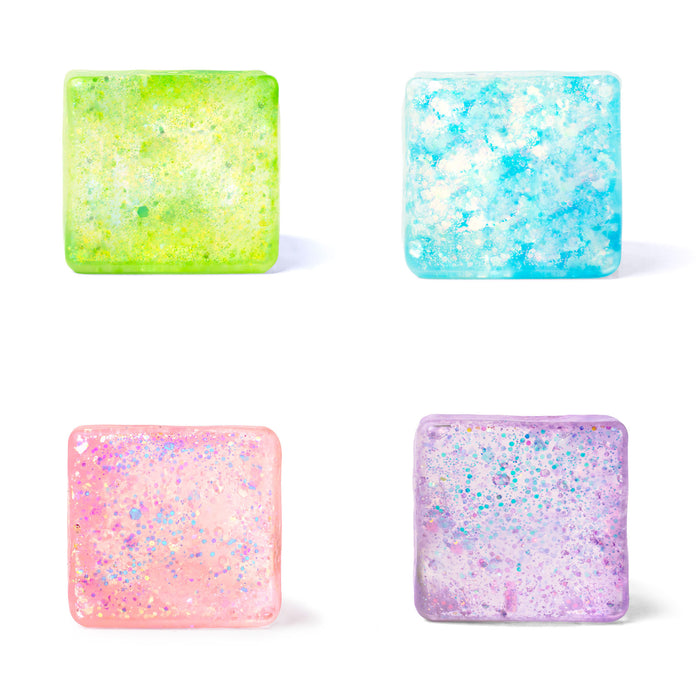 Four square translucent decorative pieces arranged in a 2x2 grid on a white background, each with rounded corners and embedded glitter. The top-left piece is lime green and yellow, the top-right is light blue and aqua, the bottom-left is pink with iridescent sparkle, and the bottom-right is lavender with multicolor glitter.