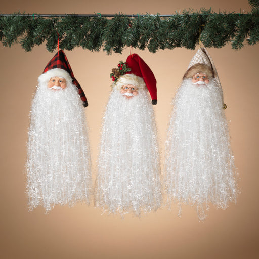 Three Santa Claus figurines hanging under a Christmas garland against a beige background
