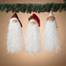 Three Santa Claus figurines hanging under a Christmas garland against a beige background