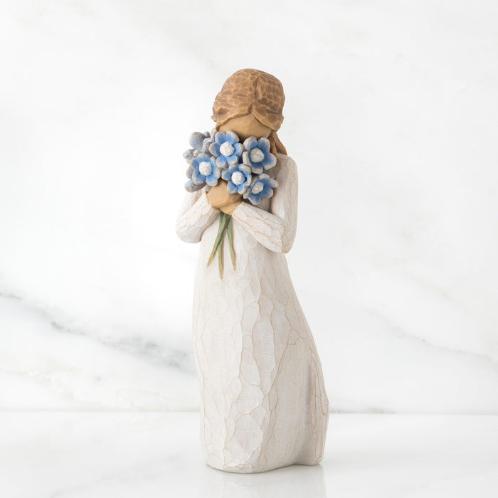 Standing figure in cream dress, holding large bouquet of blue forget-me-not flowers up to her face
