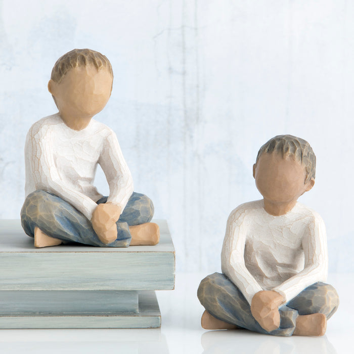 Two wooden figurines of children sitting on a white background