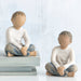 Two wooden figurines of children sitting on a white background