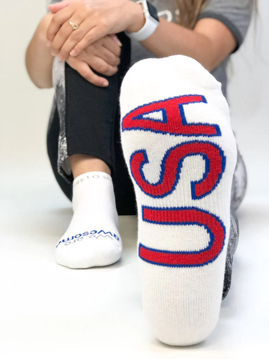 White socks with red and blue 'USA' text worn by a person sitting on a white floor.